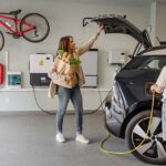 Kvinna och barn vid elbil som laddas i garage med laddbox och solpanelsystem.