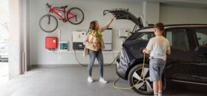 Kvinna och barn vid elbil som laddas i garage med laddbox och solpanelsystem.